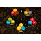 A Harmonies játék fakorongjai elrendezve a sötét játéktáblán, különböző szimbólumokkal.