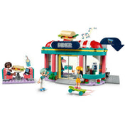 LEGO Friends 41728 Heartlake büfé – a szett belső nézete, ahol a kiszolgáló Charli ételeket ad át a pultnál, míg Aliya és Liann a vendégtérben tartózkodnak. Színes részletek, italautomata, tálalópult és falra ragasztott zenei matricák fokozzák az autentikus hangulatot.