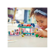 LEGO Friends 41728 Heartlake büfé játék közben – egy mosolygó gyermek játszik a készlettel otthoni környezetben. A klasszikus amerikai stílusú LEGO étterem előtt minifigurák és kiegészítők láthatók, életszerű játékszituációban.