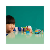 Egy kisfiú örömmel játszik a LEGO Friends Homokfutó móka (41725) készlettel. Az asztalon Liann homokfutóval, Zac szörfözve, a kiskutya pedig a közelben figyel. A háttér letisztult, zöld színű, így a jelenet még jobban kiemelkedik.