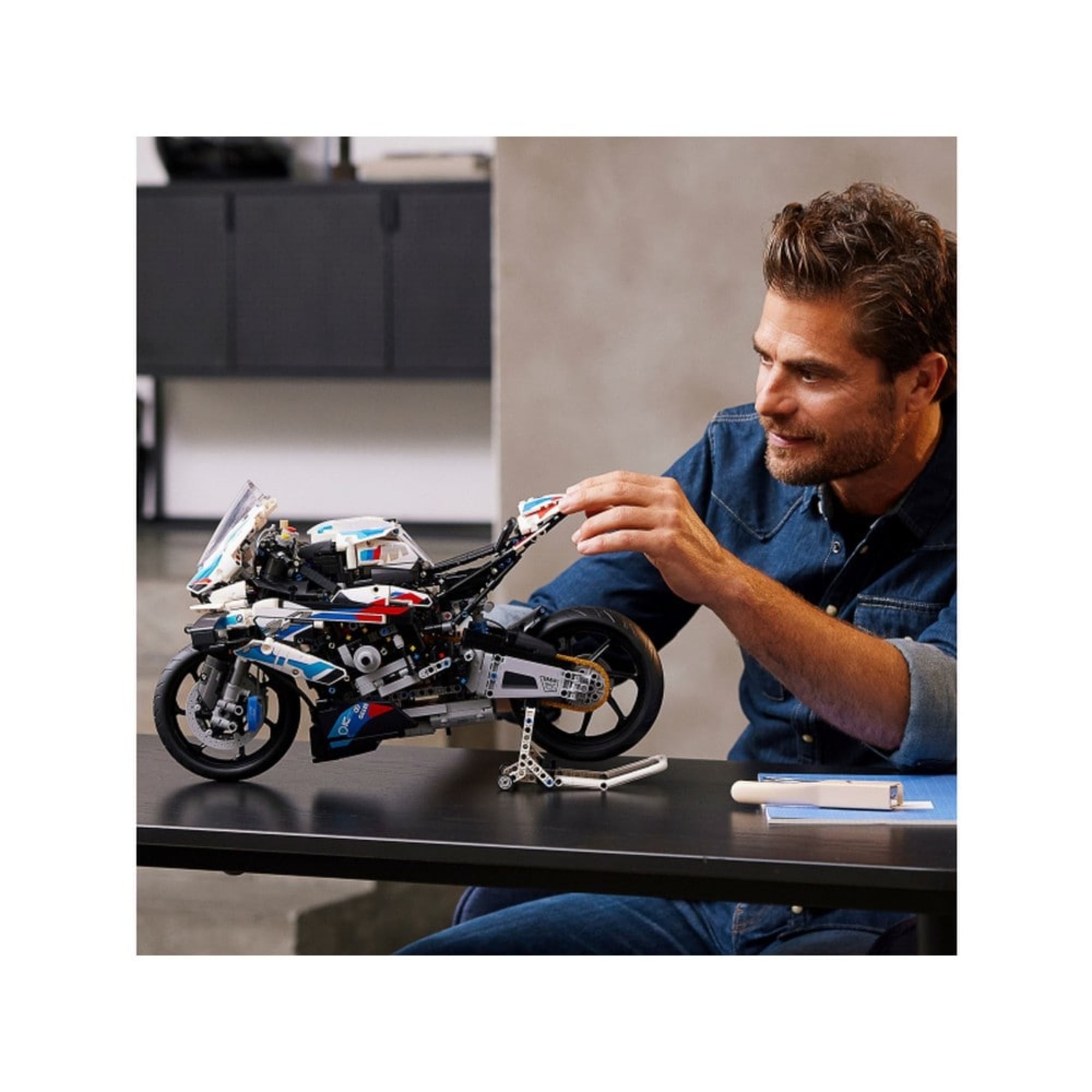 Egy férfi asztalon mutatja be a LEGO Technic BMW M 1000 RR 42130 modellt, a motorkerékpár kiállító állványon áll.
