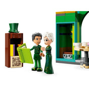 Közeli kép két karakterfiguráról a LEGO Wicked – Köszöntünk Emerald Cityben (75684) készletből, háttérben egy zöld LEGO épületrészlet, előtérben egy könyvespolc és egy zöld színű nyitott könyv.