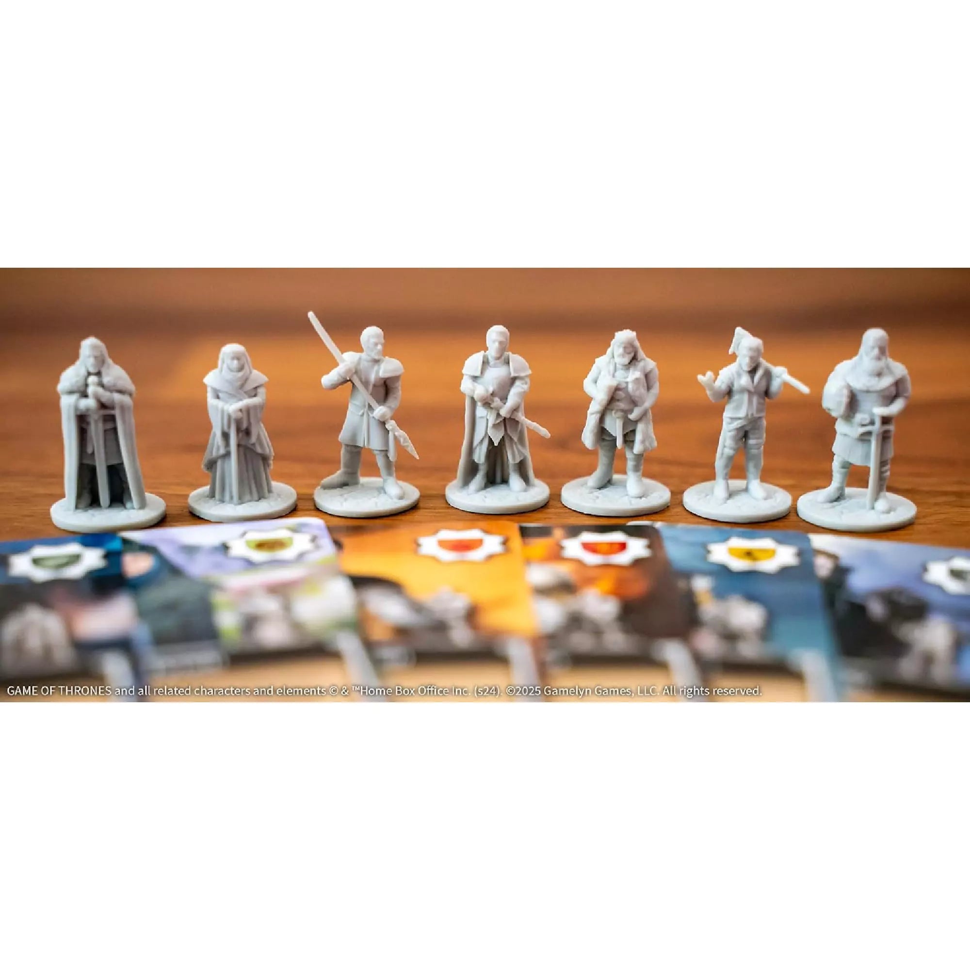 Tiny Epic Game of Thrones szürke színű karakterfigurák sorban elhelyezve, elöttük a megfelelő színes karakterkártyák részletei láthatók.