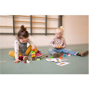 Két kisgyermek játszik a Fagyi Álom fa memóriajátékkal egy szőnyegen ülve, előttük színes fagylaltgombócok és sablonkártyák.