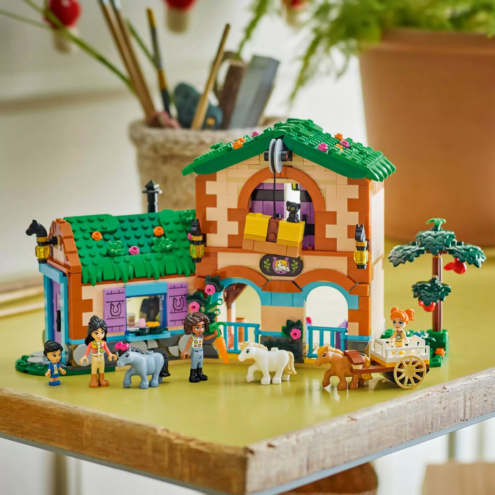 LEGO Friends Pónifarm és istálló (42654) készlet egy asztalon elhelyezve, pónikkal, kocsival és karakterekkel játék közben.