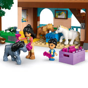 LEGO Friends Pónifarm és istálló (42654) jelenet, ahol a figurák ápolják a pónikat az istállóban, lila ládával és kiegészítőkkel.