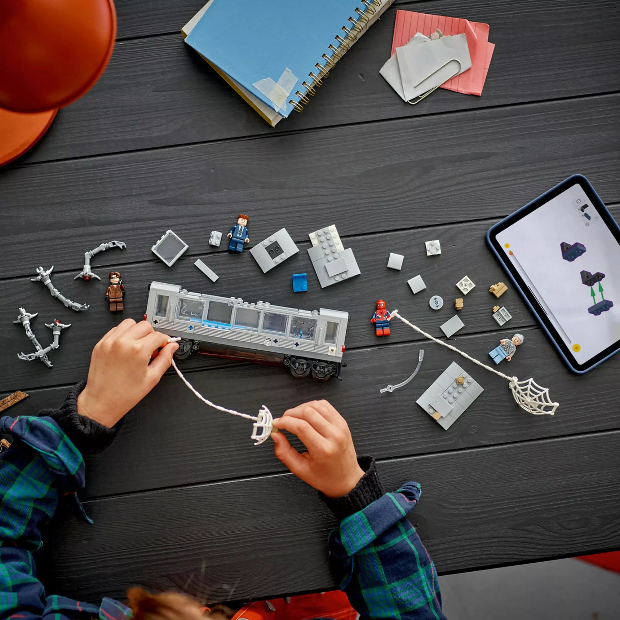 Gyerek játszik a LEGO Marvel Super Heroes: Pókember és Doc Ock csatája a metrókocsiban (76321) készlettel, szétszedett darabok és építési útmutató az asztalon.