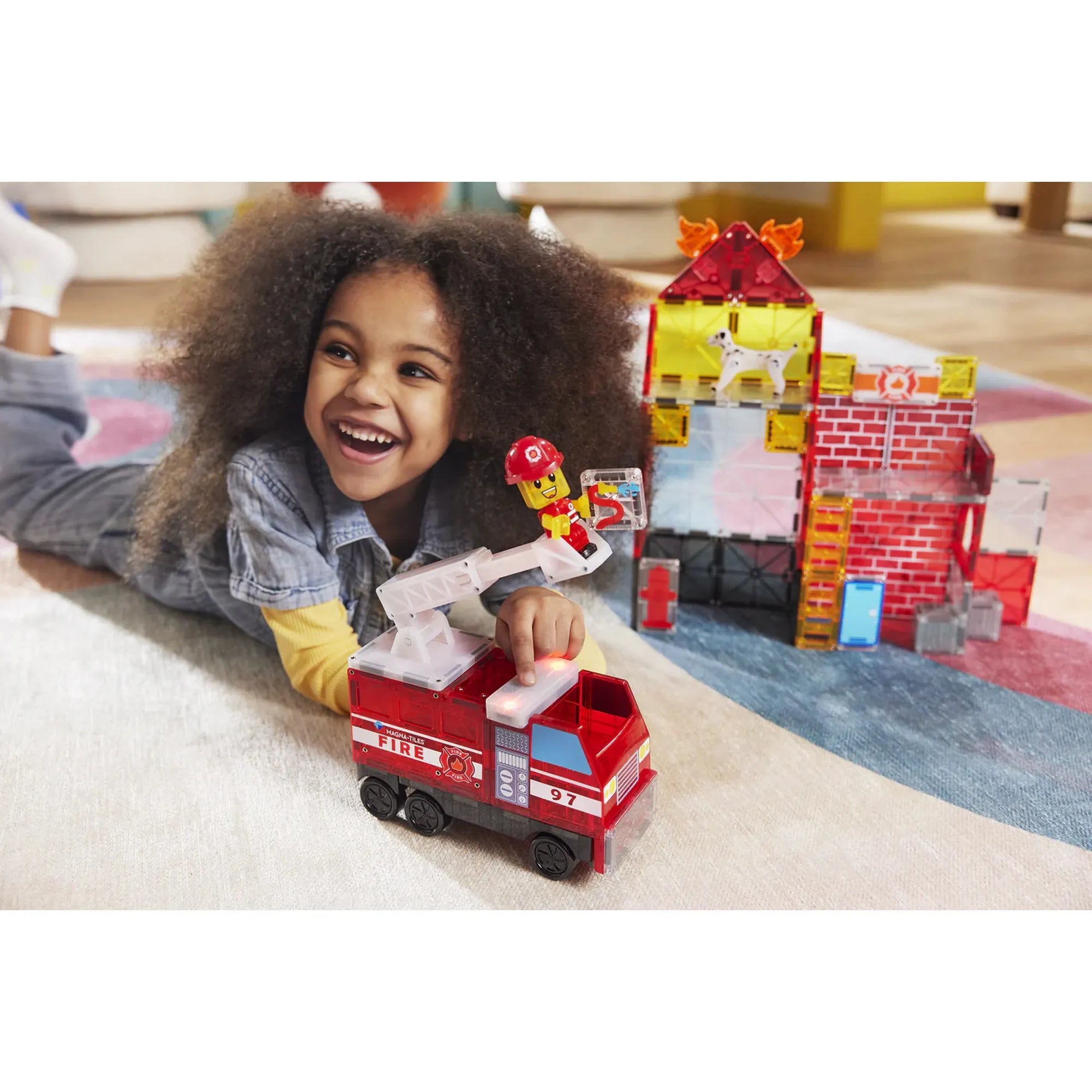 Kislány játszik a Magna-Tiles Fire Station készlettel, a tűzoltóautóval és az állomással a szobában.