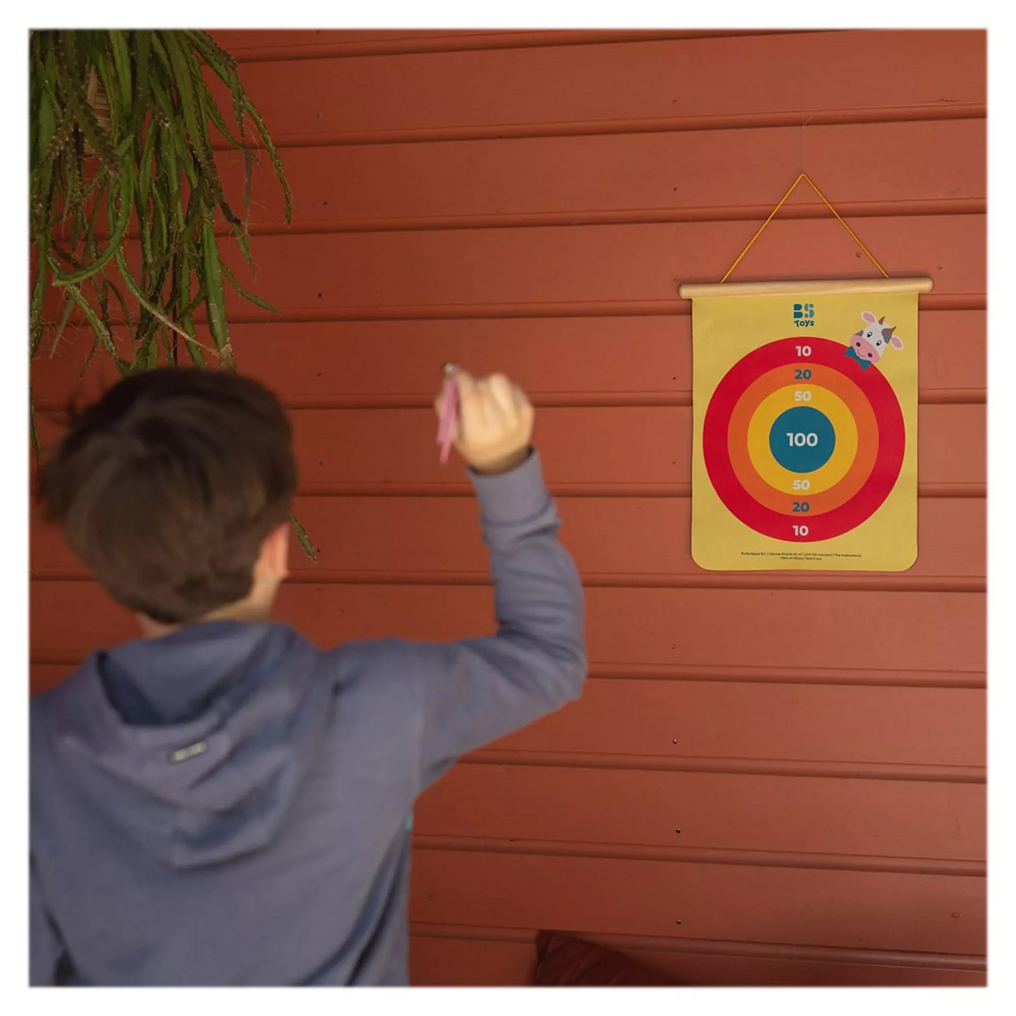 Egy fiú készül eldobni egy rózsaszín mágneses nyilat a BS Toys mágneses célbadobó sárga céltáblájára, amely koncentrikus körökből áll.