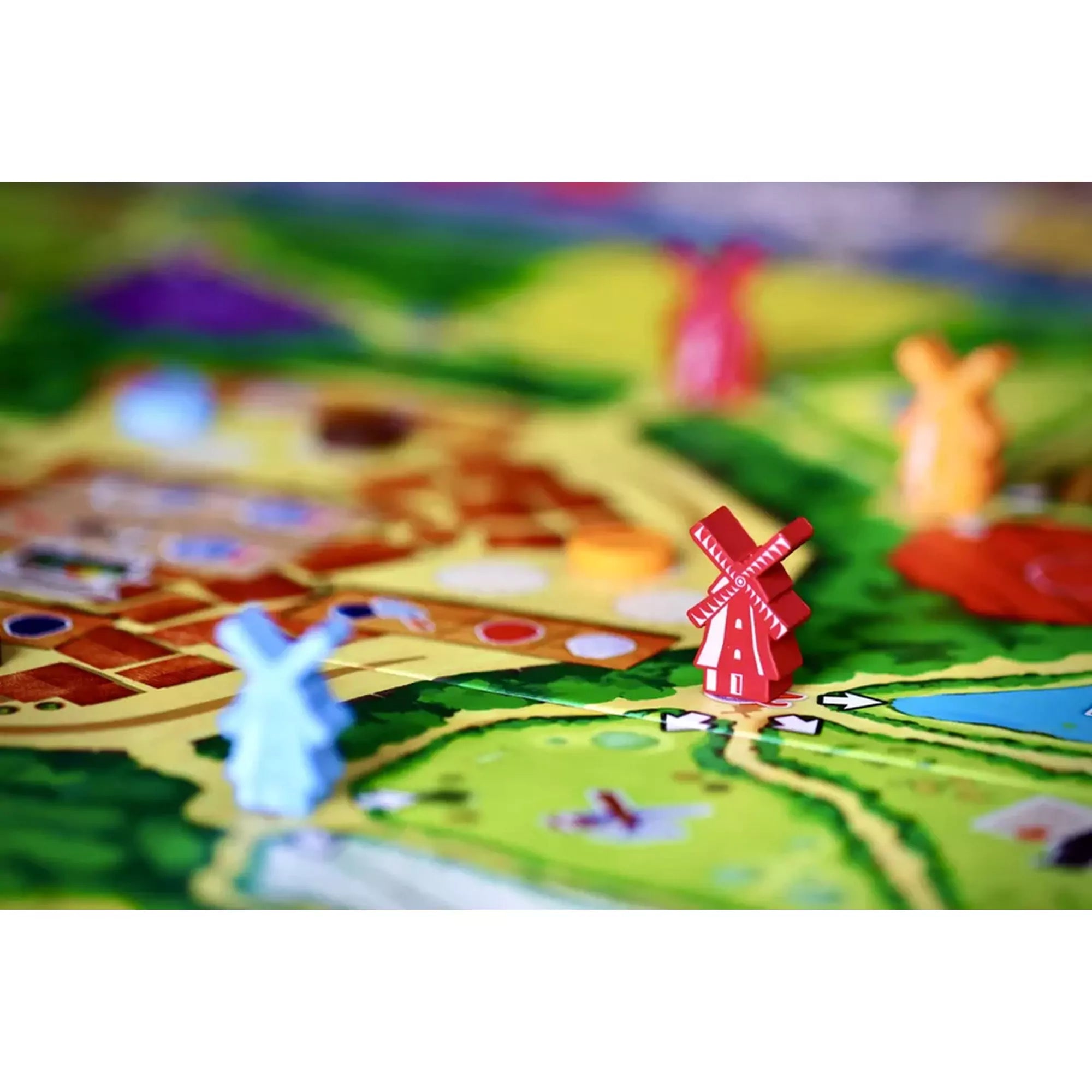 A Windmill Valley társasjáték színes szélmalom alakú bábui közelről, egy részletes játéktáblán elhelyezve.