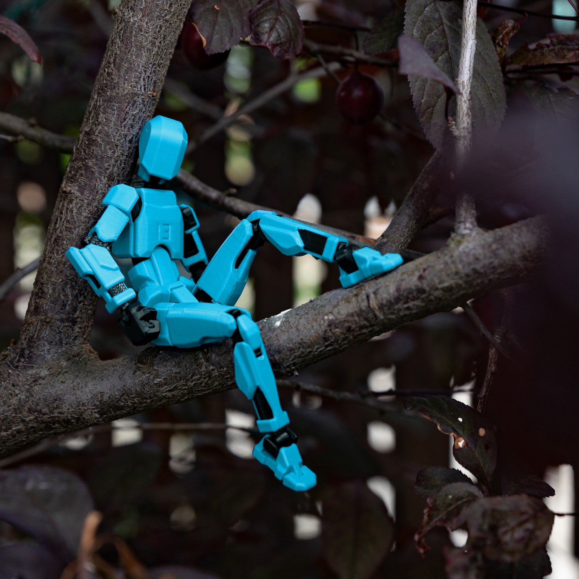 3D Robotfigura R13: Türkiz – A figura természetes környezetben, egy faágon ülve, mozgatható ízületeivel különböző pózokat felvéve.