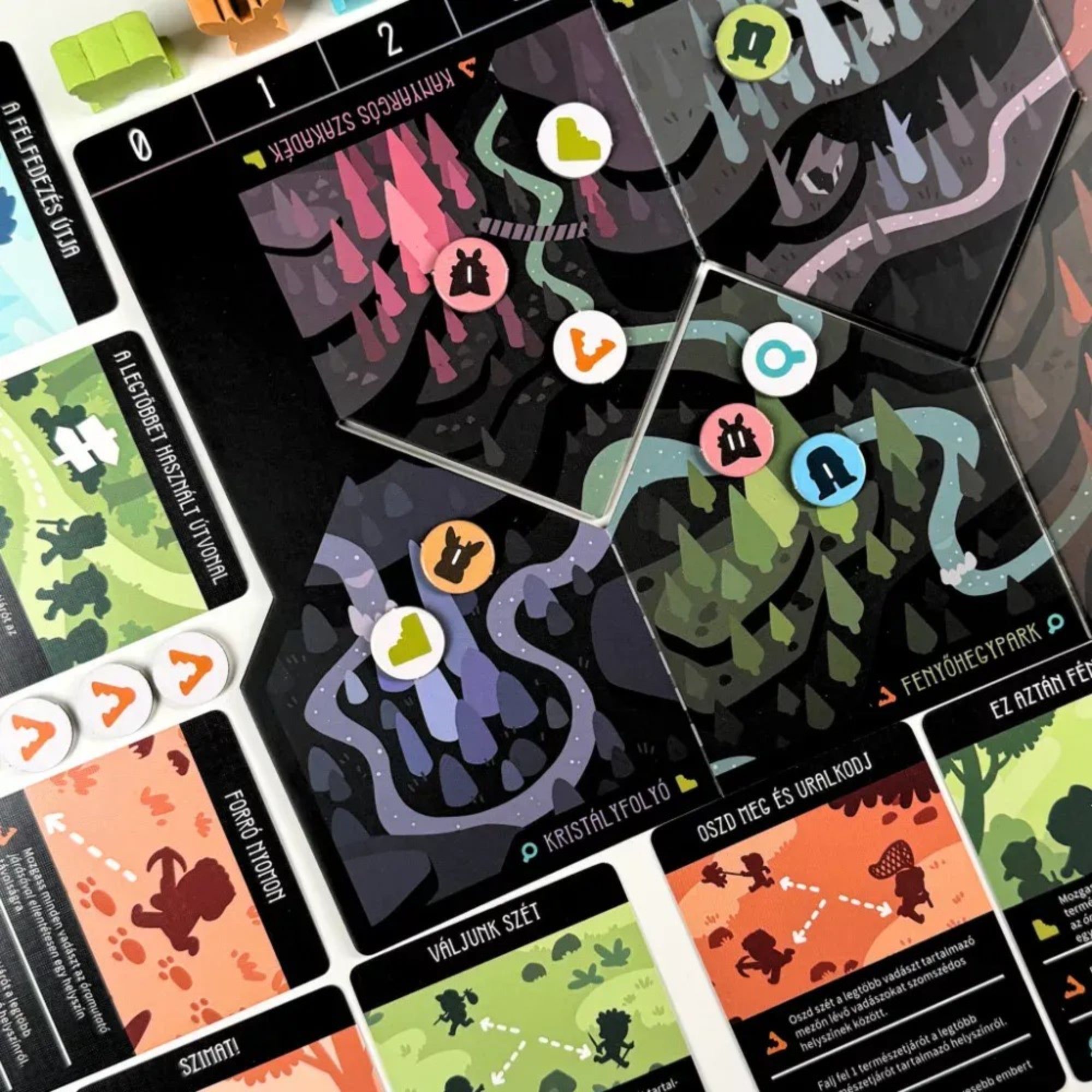 Árnybestiák játéktábla közelről, ikonokkal jelölt területekkel és színes jelölőkkel játék közbeni elrendezésben