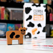 Csorda Szellem – Műüzik és Mozik társasjáték Arany Marha fafigura közelről, háttérben a játék dobozával.