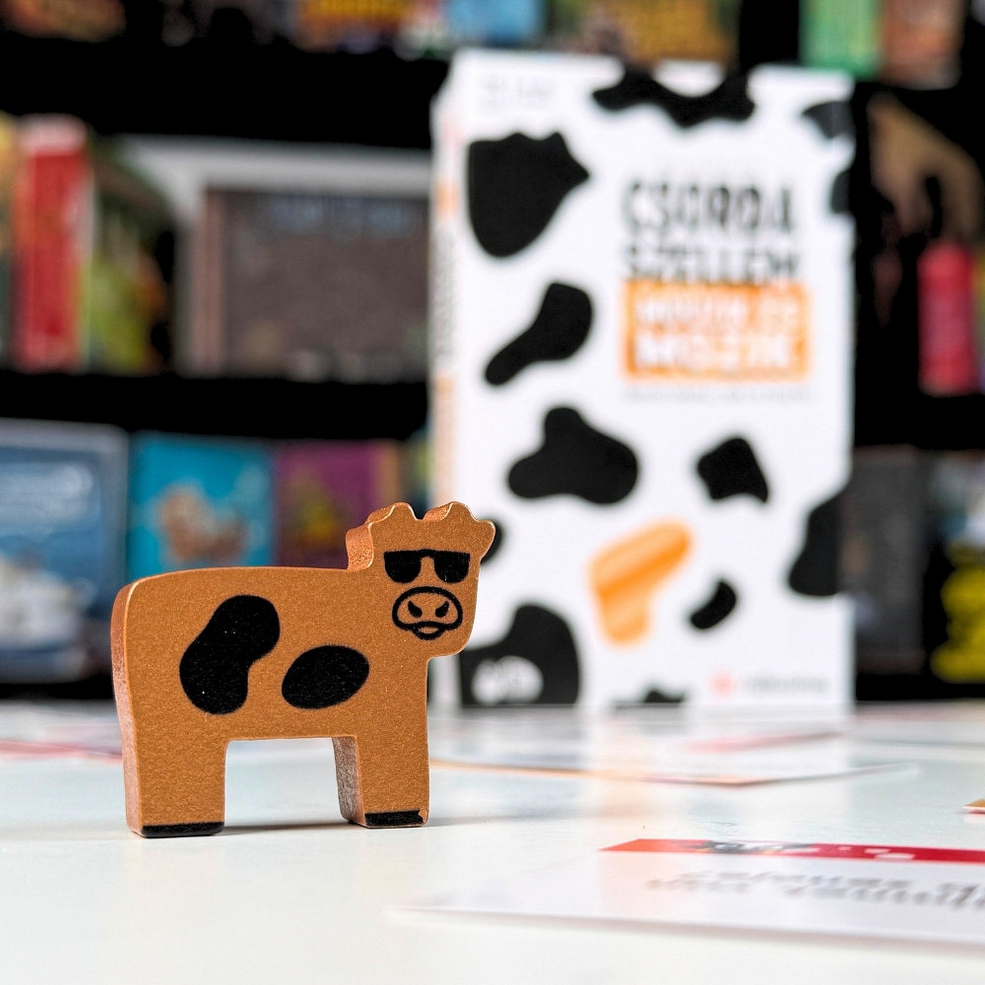 Csorda Szellem – Műüzik és Mozik társasjáték Arany Marha fafigura közelről, háttérben a játék dobozával.