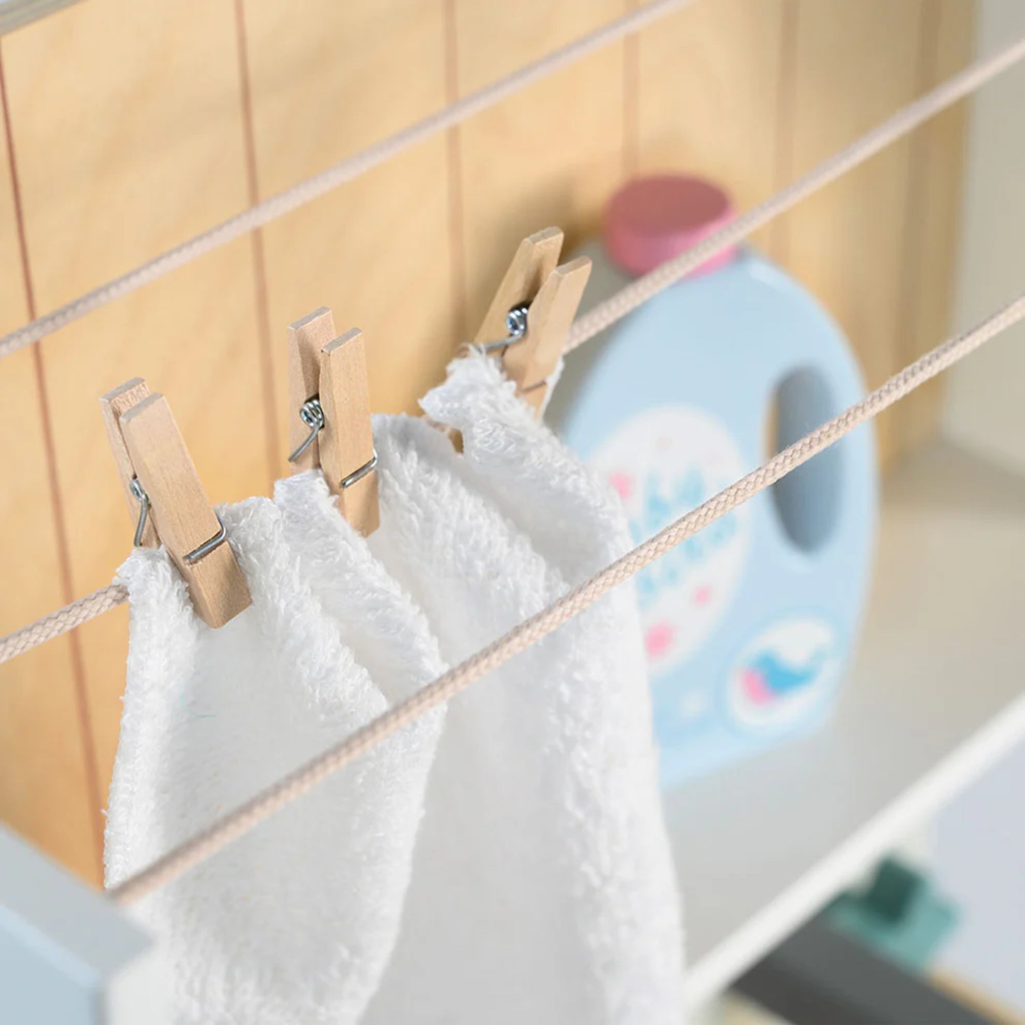 Közelkép a Tender Leaf fa mosoda szárítóköteléről, amelyen apró fa csipeszekkel rögzített fehér törölközők száradnak.

