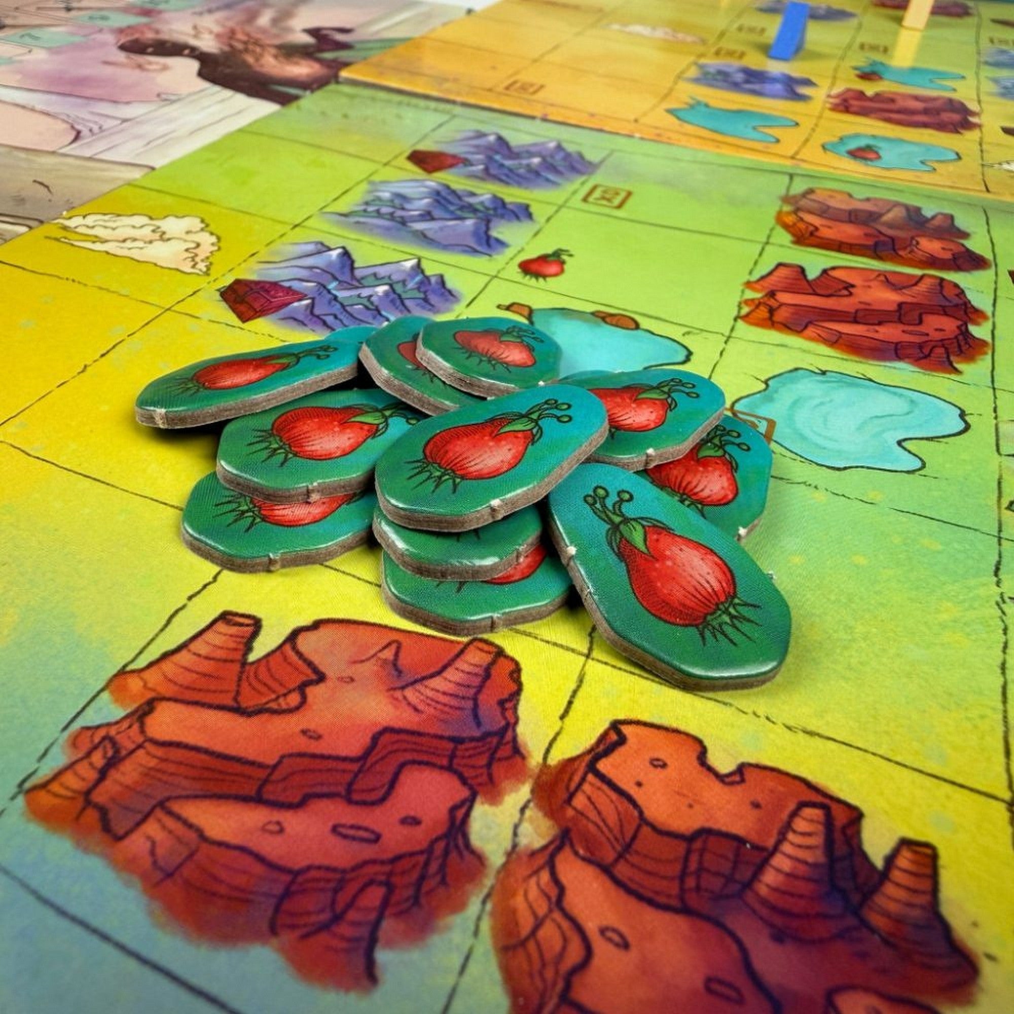 Kóborló Karaván – Gyümölcs tokenek a játéktáblán, színes mezőkön elhelyezett játékelemek közelről.