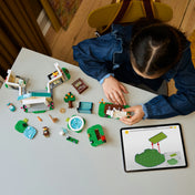 Egy gyermek épp építi a LEGO Animal Crossing 77056 készletet. Az asztalon szétszórva láthatók a külön modulok, figurák, zöld alaplapok és egy tablet a digitális útmutatóval – valós játékélmény és interaktív tanulás.