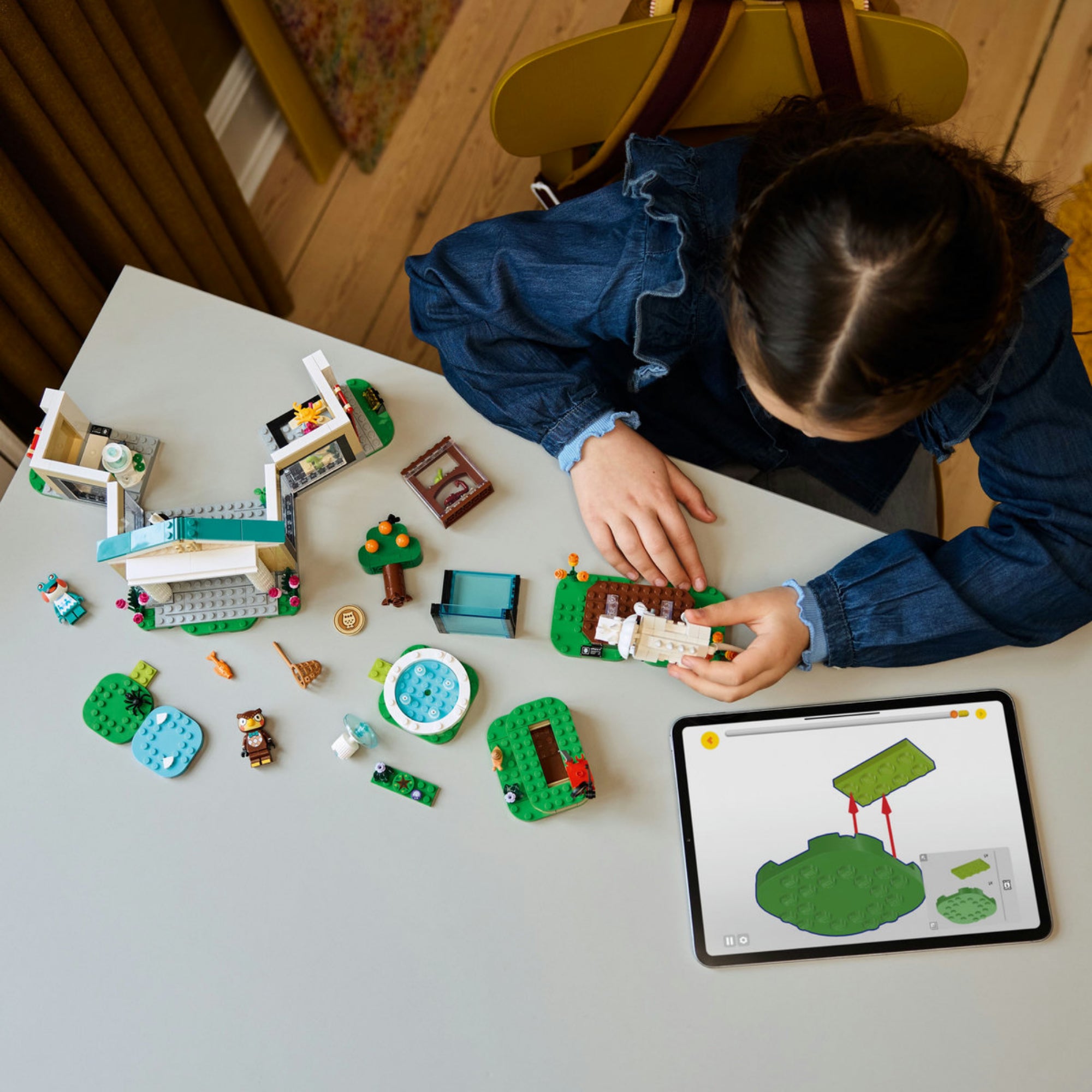 Egy gyermek épp építi a LEGO Animal Crossing 77056 készletet. Az asztalon szétszórva láthatók a külön modulok, figurák, zöld alaplapok és egy tablet a digitális útmutatóval – valós játékélmény és interaktív tanulás.