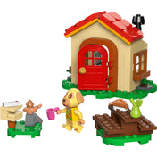 LEGO Animal Crossing Goldie otthonos házikója (77058) teljes készlet, amely tartalmazza a piros ajtós kis házat, Goldie figurát rózsaszín bögrével, postaládát levelekkel, kültéri pihenősarkot croissant-nal és körtével, valamint egy szökőkutat és egy madáritatót.