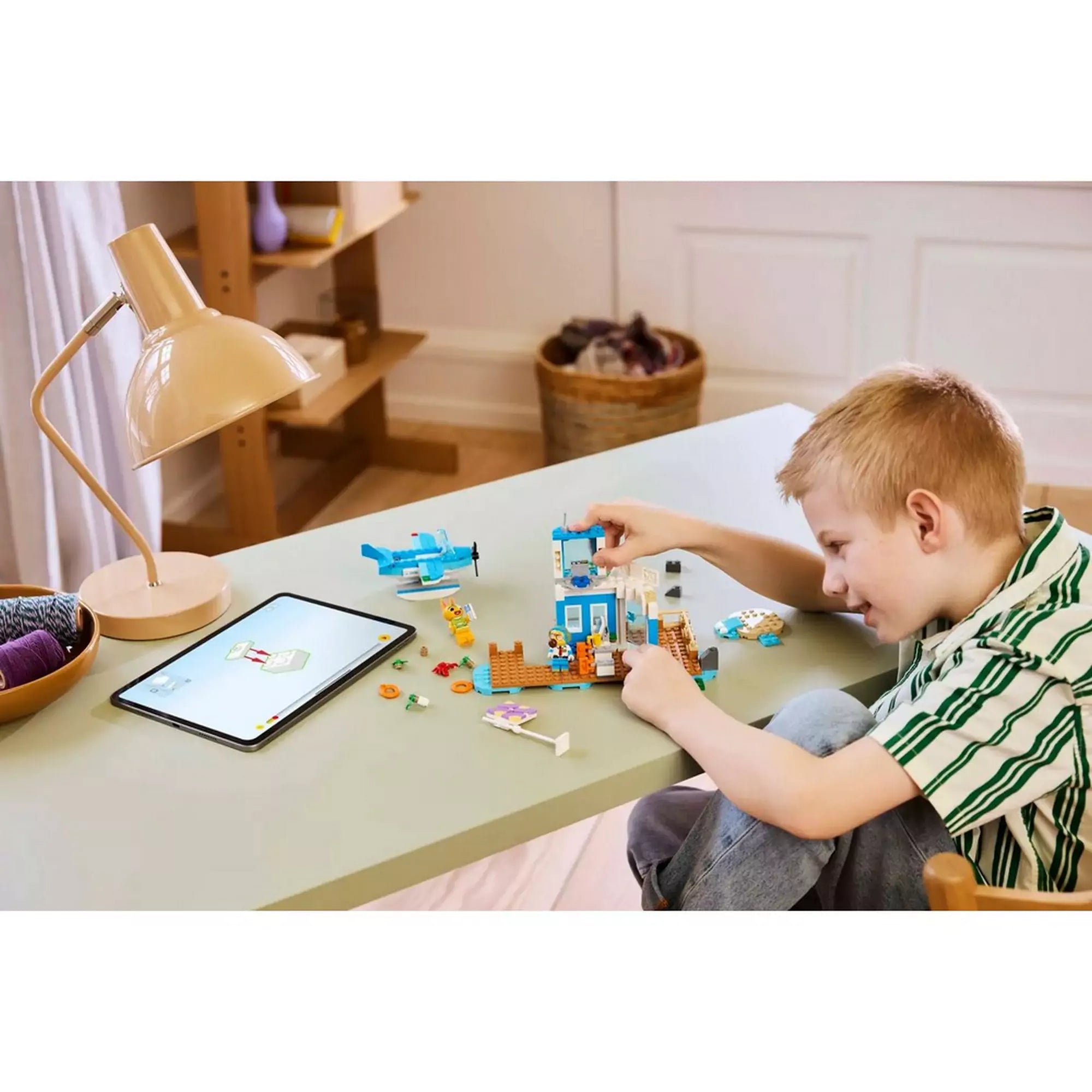 Kisfiú épp építi a LEGO Animal Crossing: Repülj a Dodo Airlines fedélzetén (77051) szettet egy asztalon, mellette tablet mutatja az útmutatót.