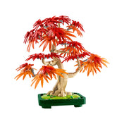 A japán juharfa LEGO-ból épített részletei látszanak közelről. A hajlított barna törzs természetes, organikus formát alkot, a levelek szélesen elterülnek, mintha egy valódi fa lenne. A zöld alapon kis díszítőelemek egészítik ki az összhatást.