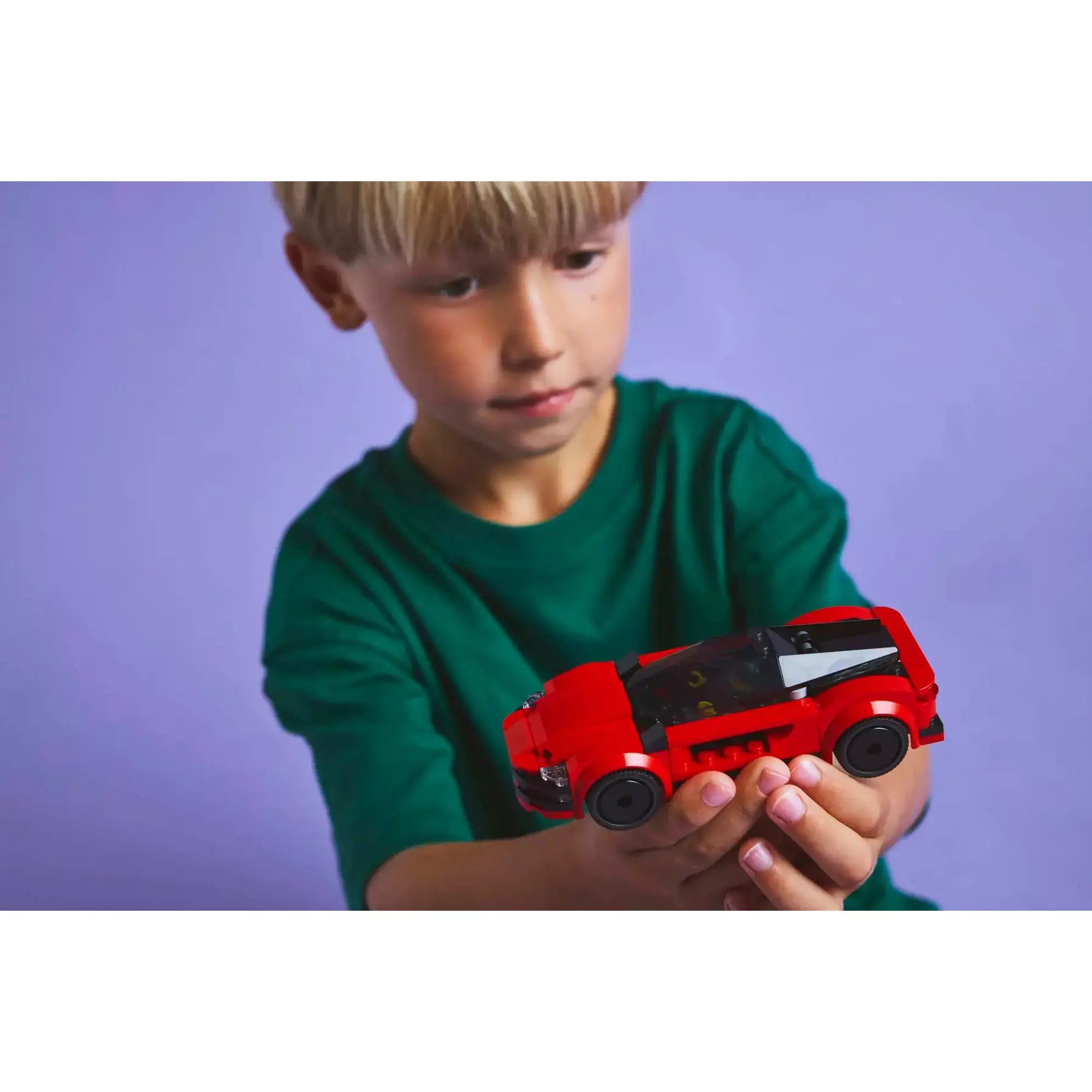 Egy fiatal fiú tartja a LEGO CITY Piros sportautót (60448), megcsodálva annak részleteit és szórakoztató funkcióit.