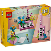 A LEGO Creator 3 az 1-ben Írógép virágokkal 31169 doboza látható, a készlet három különböző építhető modellt mutat be: egy virágokkal díszített írógépet, egy virágos állványos gitárt és egy virágcserepet tollal és jegyzetfüzettel. A doboz színes, figyelemfelkeltő dizájnnal készült, ami az alkotás örömét hivatott hangsúlyozni.