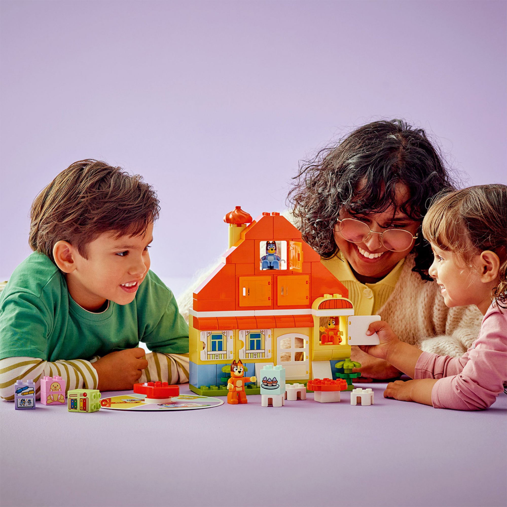 Két gyermek és egy felnőtt együtt játszik a LEGO DUPLO Bluey családi ház készlettel.
