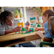 Két gyermek játszik a LEGO Minecraft 21249 készlettel egy asztalon; a jelenet élő játékhelyzetet mutat, ahol a gyerekek interakcióba lépnek a tornyokkal és minifigurákkal. A háttérben beltéri növények és meleg színek teszik barátságossá a jelenetet.
