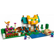 Részletes kép a LEGO Minecraft Crafting láda 4.0 (21249) készletről, ahol a készletből épített két különálló torony látható – az egyik sárga TNT-vel, a másik kék-fehér színű, tetején egy macskával. Előtérben több figura, növényzet és játékbeli jelenet is megjelenik.