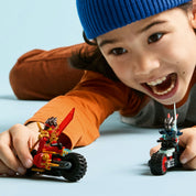 Egy kisfiú örömmel játszik a LEGO Ninjago motoros figurákkal, az egyik kezében Kai karaktere, a másikban a gonosz motoros, világoskék háttér előtt.