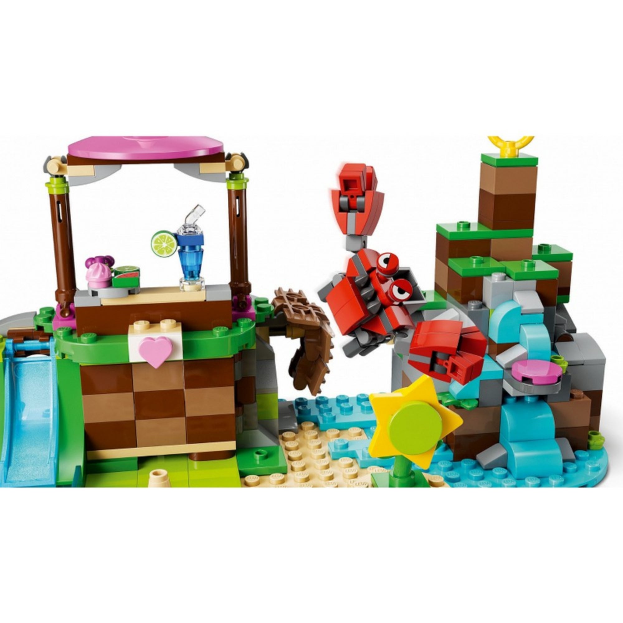 A LEGO 76992-es készlet egyik díszlete, amelyben egy piros rák figura támad egy sziklás vízesés mellett, a bal oldalon egy italos pult és egy szív díszítésű emelvény látható.