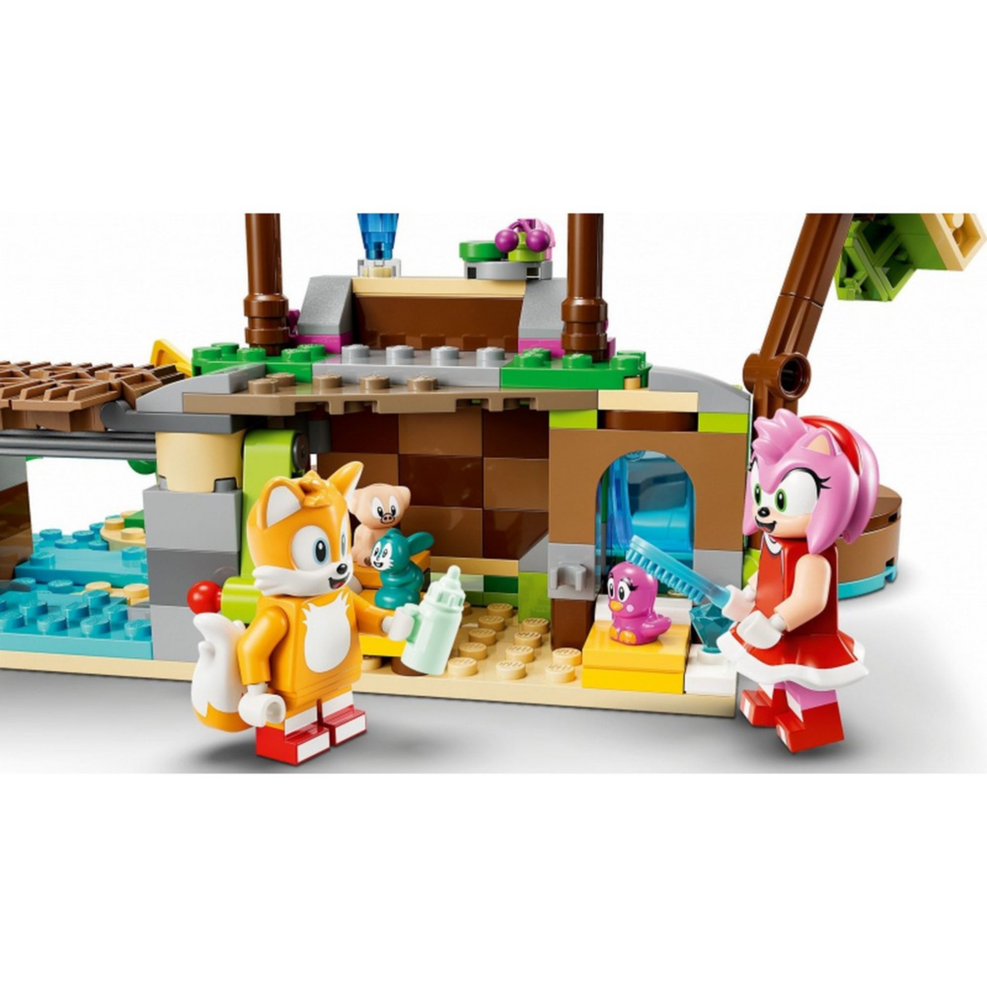 Amy és Tails LEGO-figurák kisállatokat gondoznak a LEGO 76992-es Amy állatmentő szigete készletből, háttérben épített kunyhó, bejárat, homokos rész és kisállatok.