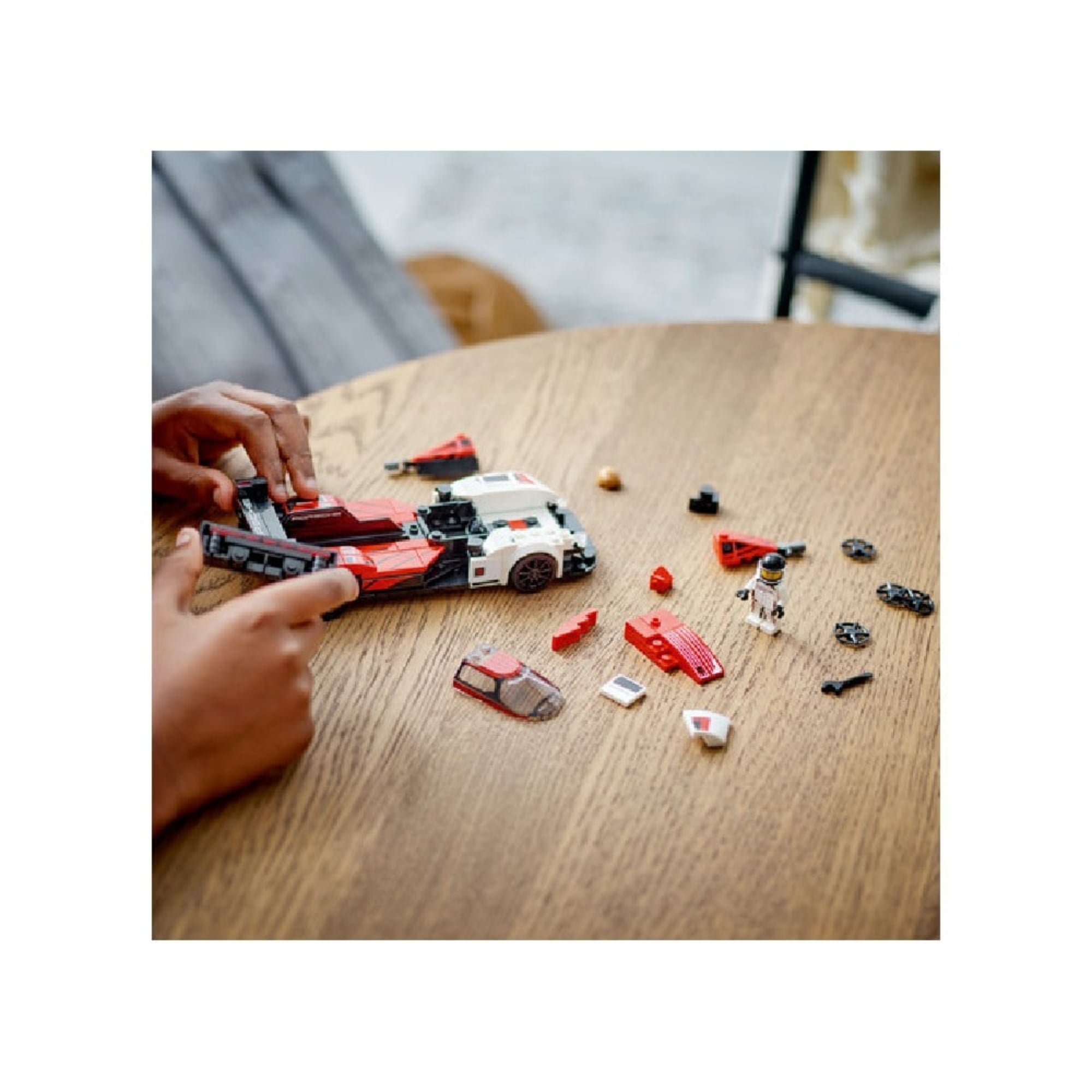 Egy gyermek egy kerek asztalon építi a LEGO Porsche 963-at, a kocsi eleje már elkészült, a hátsó részen szétszórt alkatrészek láthatók.