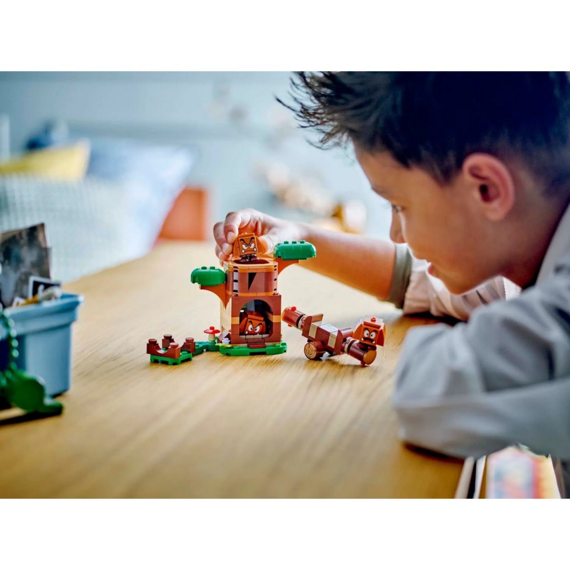 Egy fiú játszik a LEGO Super Mario Goomba játszótér (71433) készlettel, miközben a Goomba figurákat mozgatja a fa építmény körül.