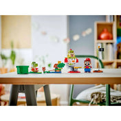 A LEGO Super Mario 71439 készlet asztalra kiállítva, elöl Mario és Yoshi, hátul Bowser Jr. Clown Car repülője, a célzászlóval és pályaelemekkel, világos szobabelsőben.
