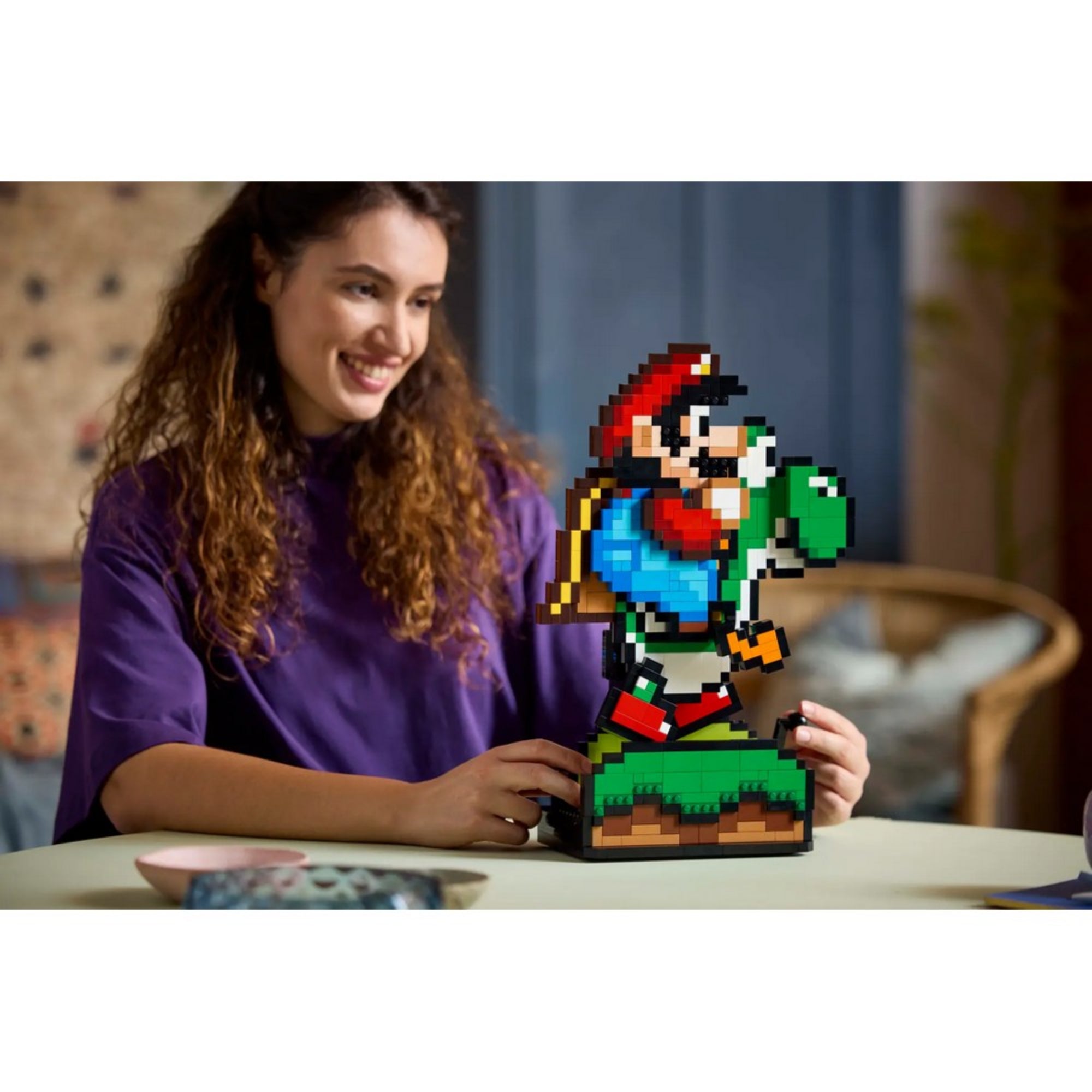 Egy nő mosolyogva játszik a LEGO Super Mario – Mario és Yoshi szett kész figurájával egy asztalnál.