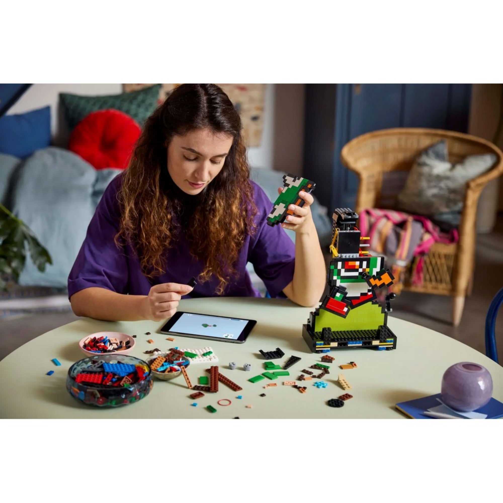 Egy fiatal nő tablet segítségével építi össze a LEGO Super Mario 71438 szettet, a darabok szétszórva az asztalon.