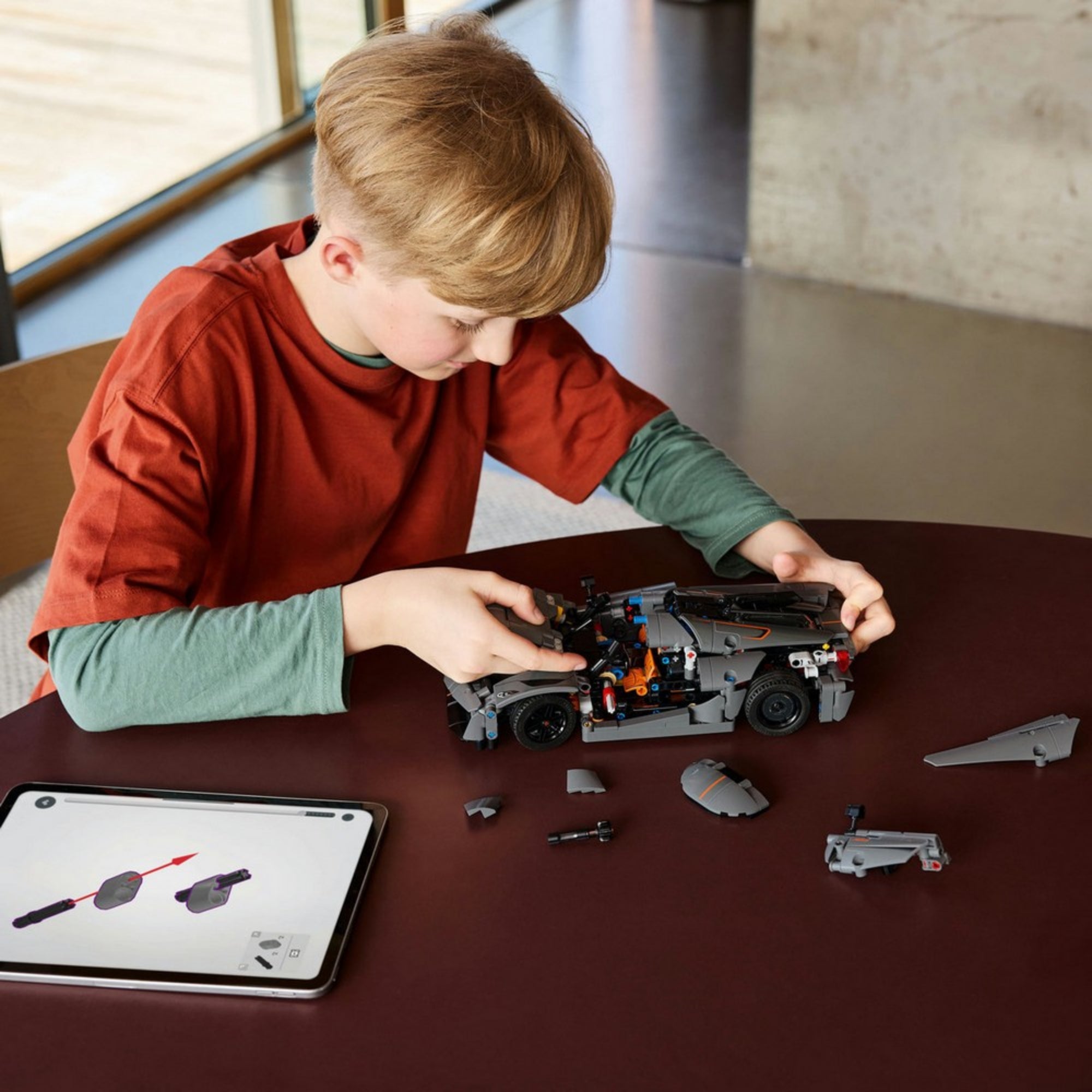 Fiú szereli össze a LEGO Technic Koenigsegg Jesko autót lépésről lépésre egy tablet segítségével, a darabok rendszerezve előtte az asztalon.