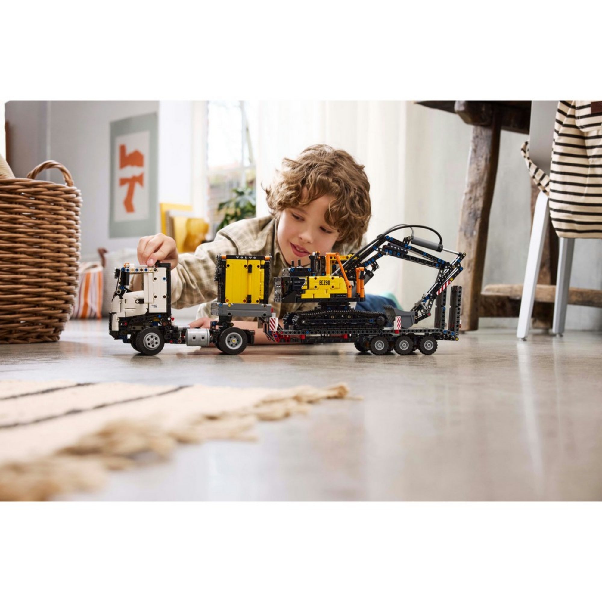 Egy kisfiú játékközben a LEGO Technic Volvo FMX és EC230 készlettel, a padlón játszva irányítja a járműveket.