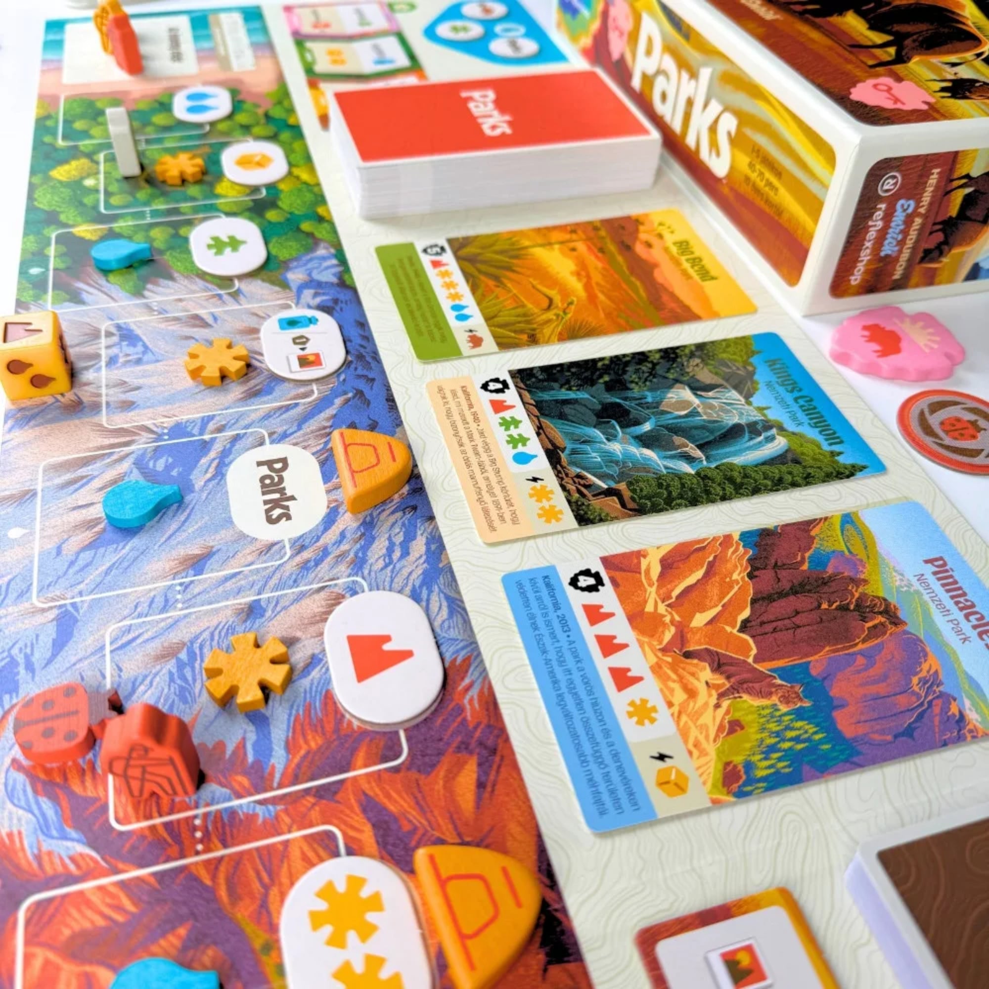 Parks társasjáték játékmenet közben, túraútvonal táblával, park kártyákkal, jelölőkkel és paklikkal egy részletes asztali elrendezésben.