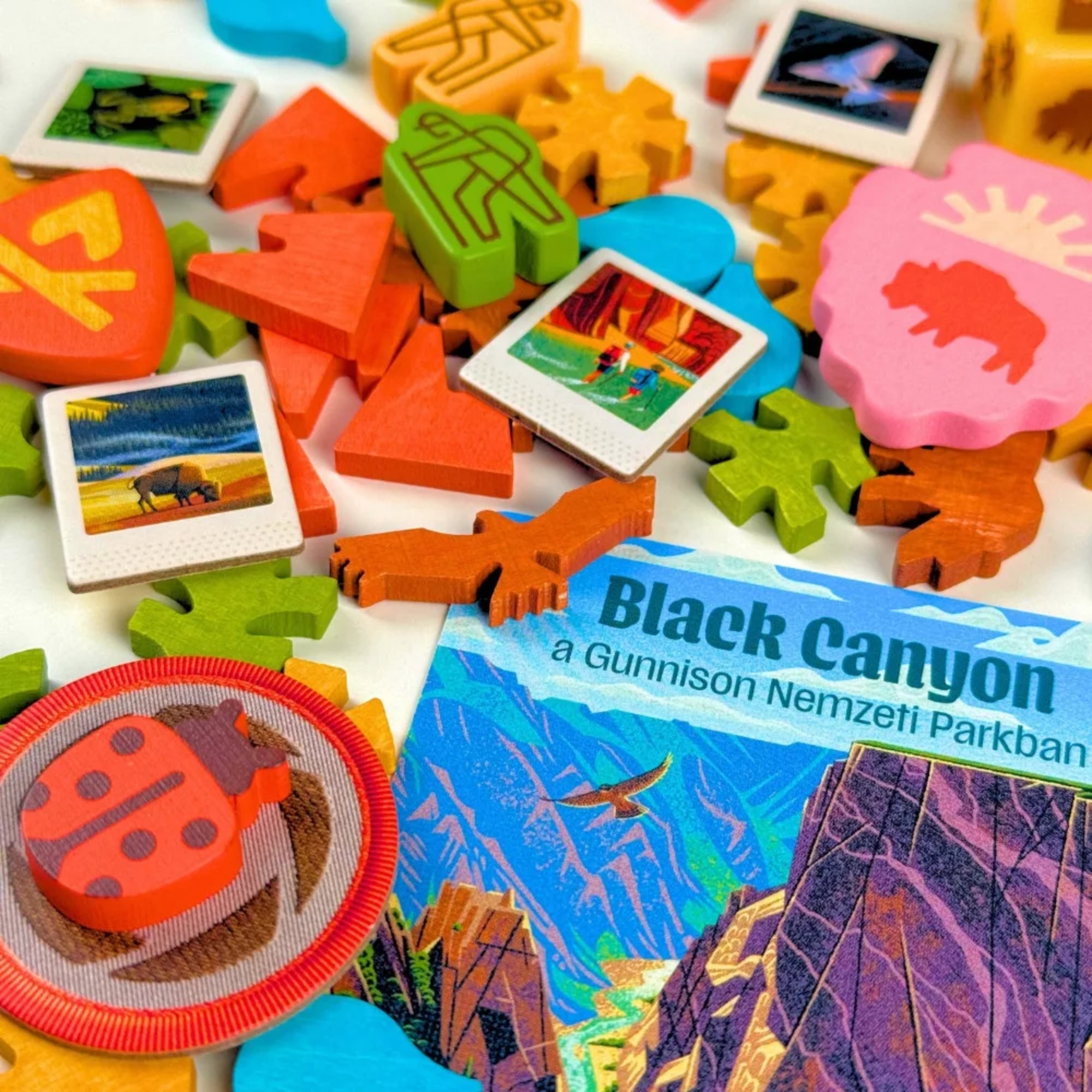 Parks társasjáték színes fa jelölői közelről, állat- és természet ikonokkal, valamint nemzeti park kártyarészlettel (Black Canyon).