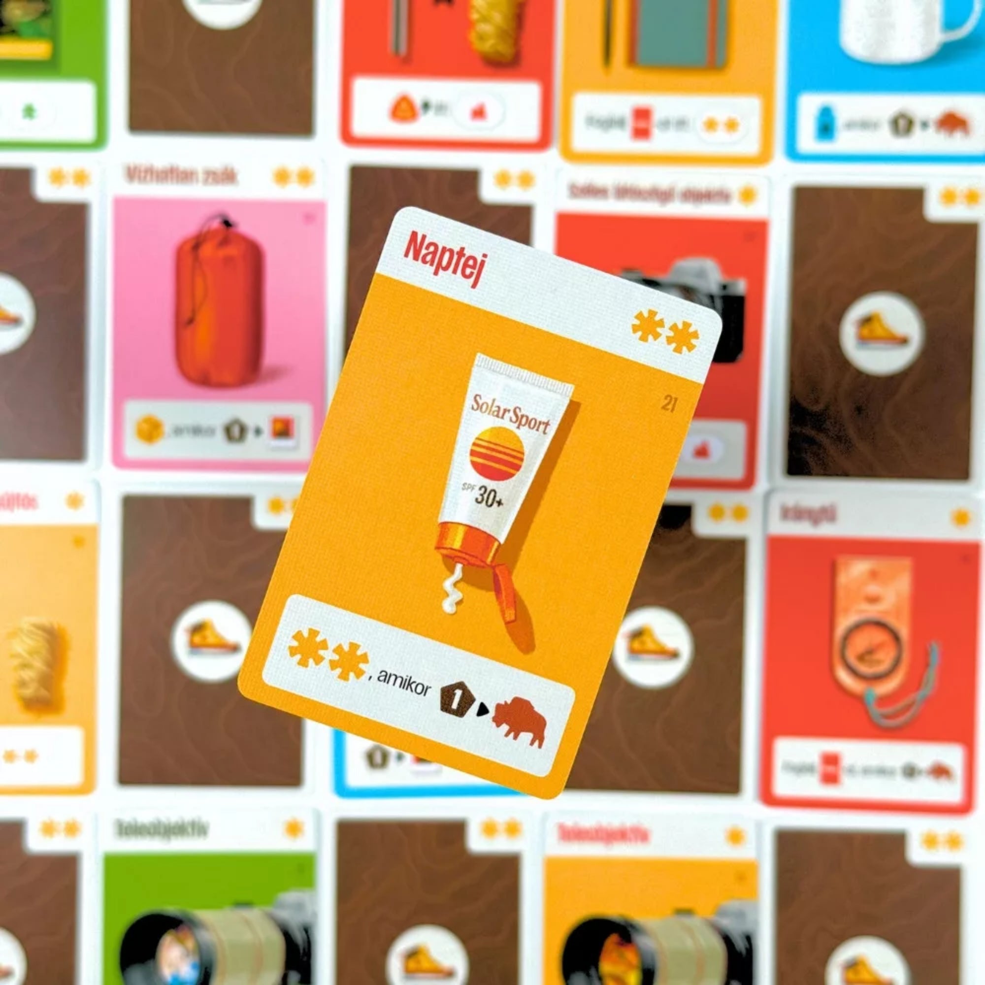 Parks társasjáték „Naptej” felszerelés kártya kiemelve, háttérben további felszerelés- és tárgykártyák elmosódva.