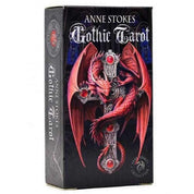 A képen az Anne Stokes Gothic Tarot pakli doboza látható. A borítót egy lenyűgöző, vörös sárkány díszíti, amely egy gótikus kereszt köré tekeredett. A keresztet vörös ékkövek ékesítik, amelyek drámaian kiemelkednek a fekete háttérből. A művészi borító a pakli sötét, misztikus és fantasy hangulatát tükrözi. A doboz oldalán a pakli neve és a művésznő aláírása is szerepel, jelezve, hogy ez az Anne Stokes Collection része.