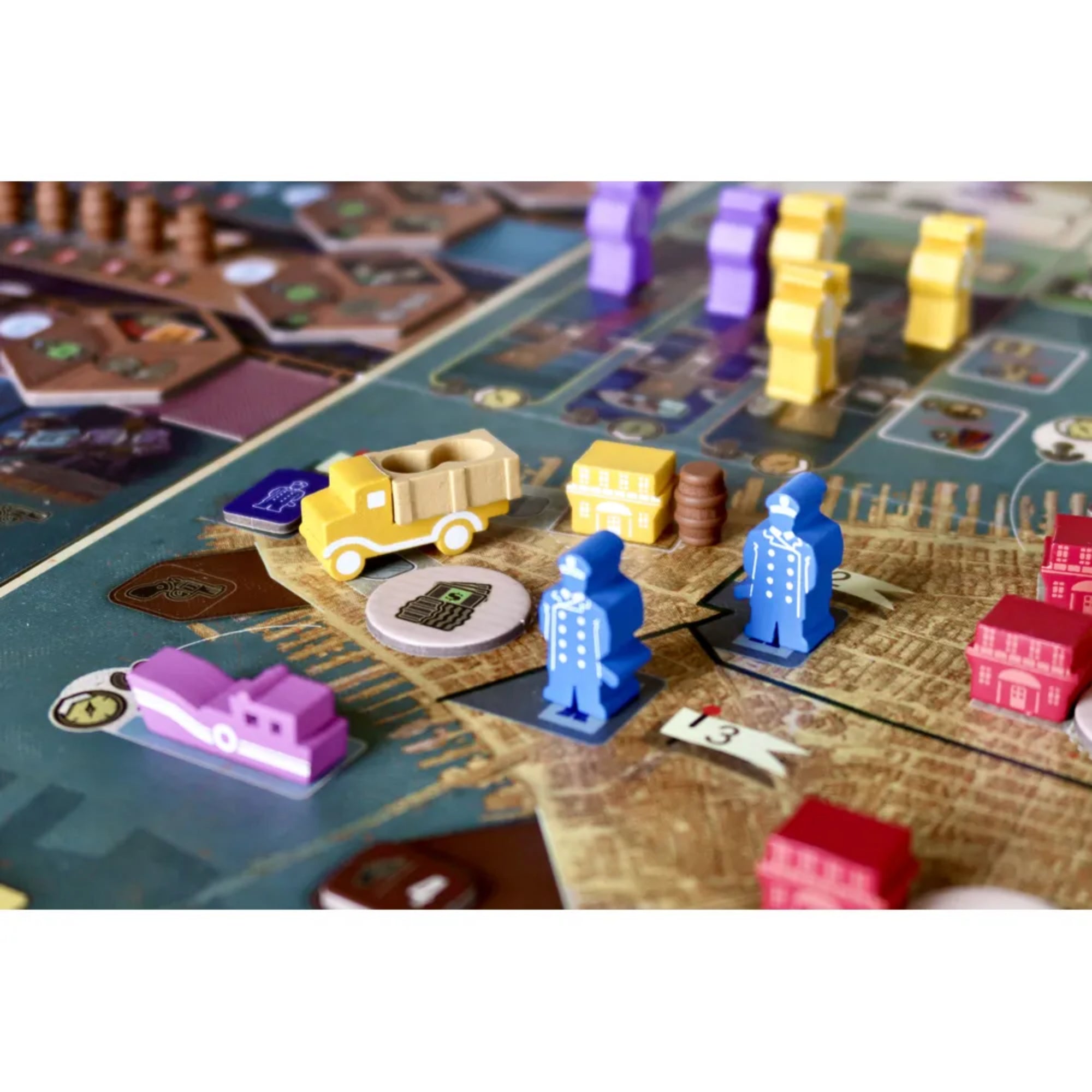 Közelkép a Zugkocsma társasjáték komponenseiről: kék karakterfigurák, sárga autó, épületek és jelölők a részletes várostérképen.