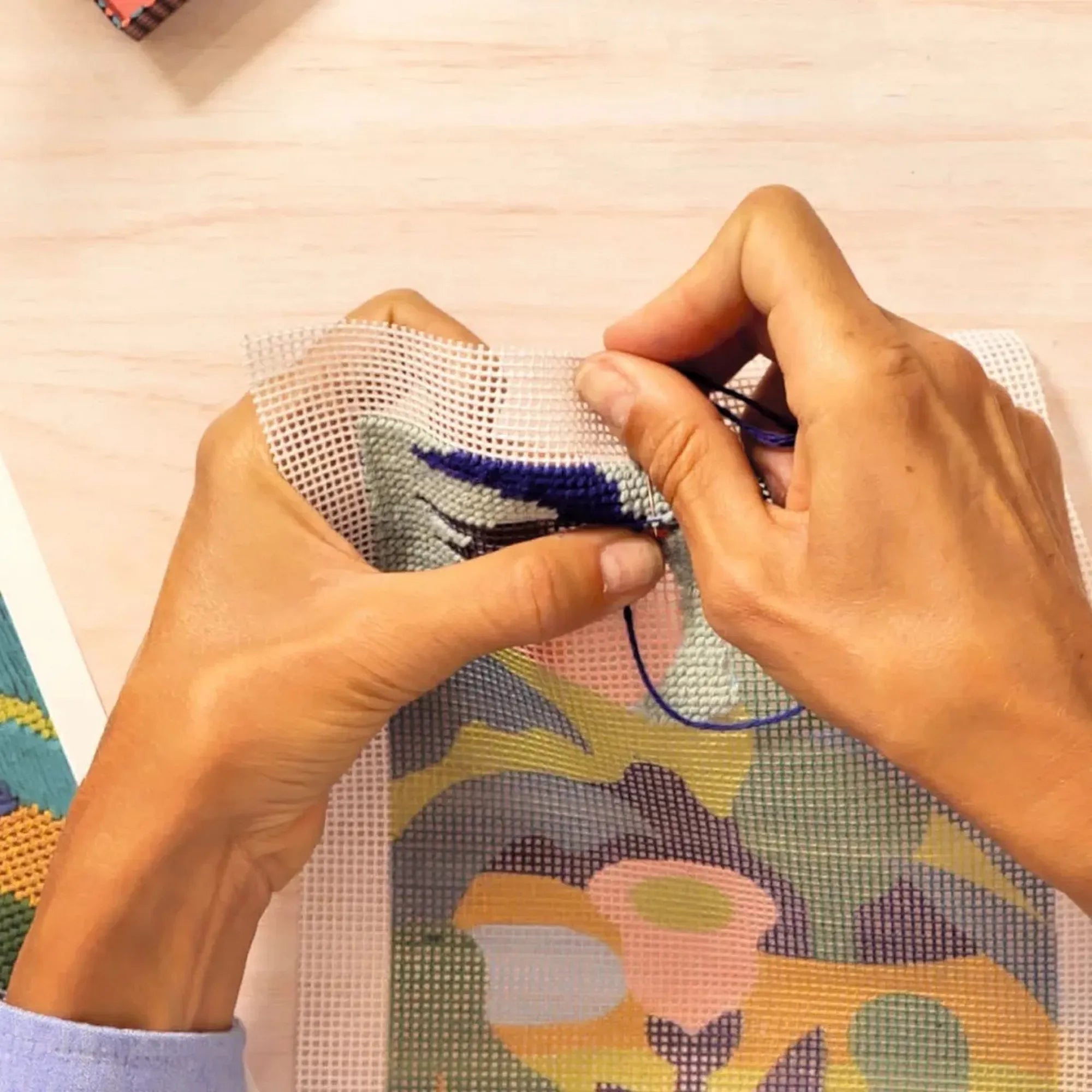 Atelier 65 hímzőkészlet – kézben tartott vászon, amelyre a felhasználó kék fonallal hímez.