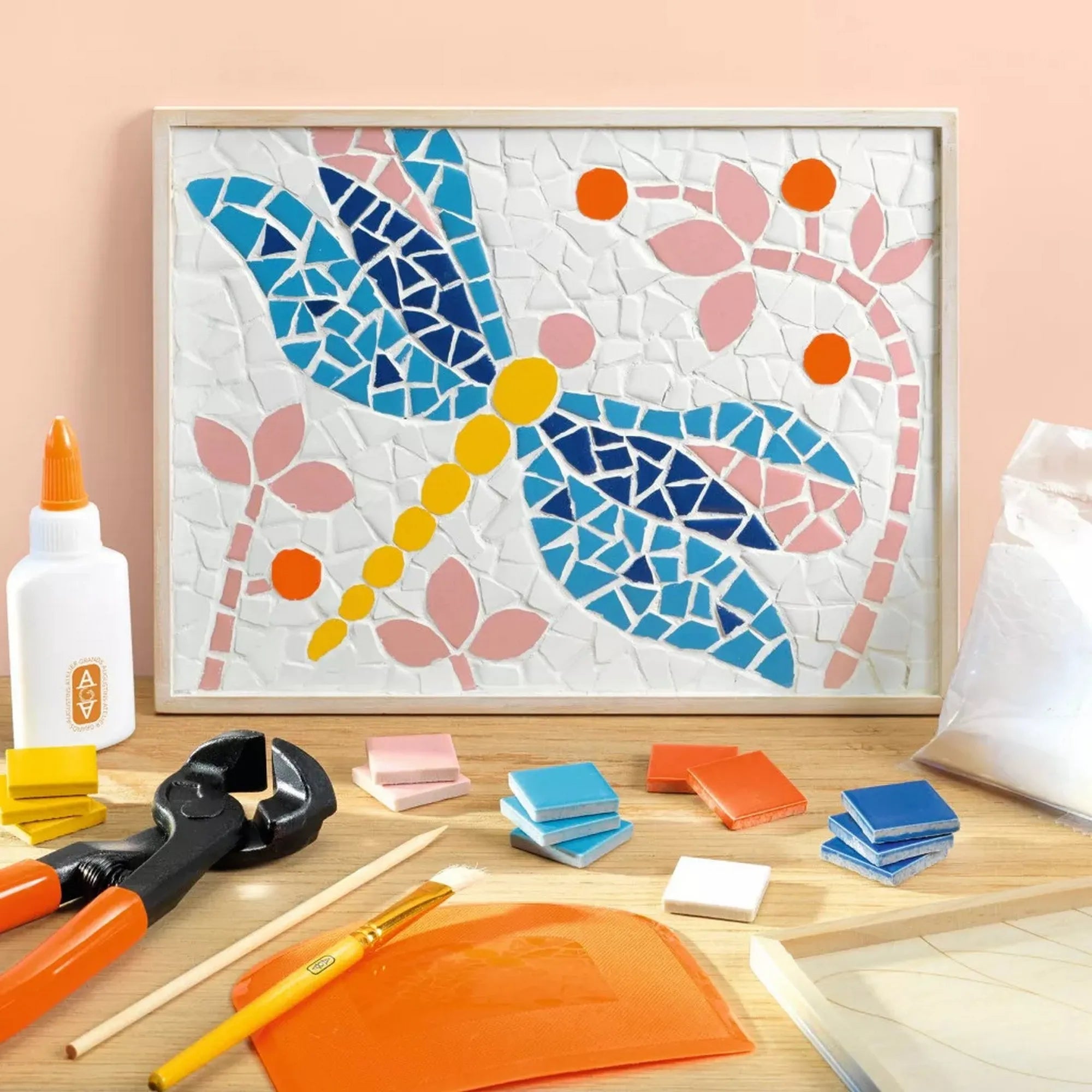 Atelier 72 mozaikkészítő felnőtteknek: Szitakötő – elkészült szitakötő mozaikkép virágmotívumokkal, az alkotáshoz használt eszközökkel körülvéve.