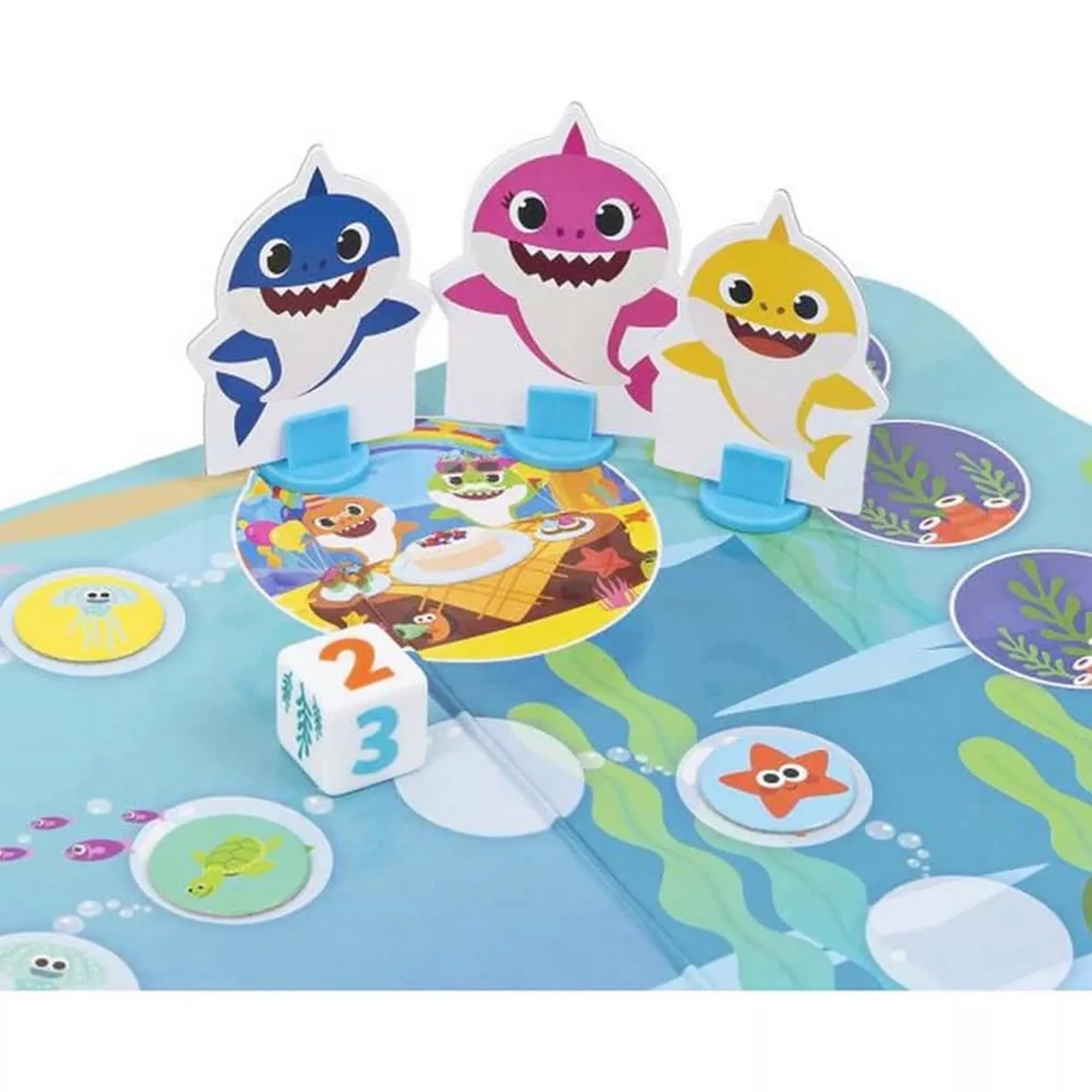Három cápakarakter – a kék, a rózsaszín és a sárga Baby Shark – a pálya céljához közel, egy dobókocka mellett. A játékmezőn aranyos tengeri állatok, buborékok és színes körök láthatók.