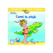 „A Conni la plajă román nyelvű mesekönyv borítója, amelyen Conni piros fürdőruhában áll a tengerparton, kezében zöld felfújható krokodilját, Fridolint tartva.”