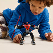Egy kisfiú figyelmesen játszik a teljesen megépített Darth Maul mecha figurával, amely vörös fénykardot tart a kezében.
